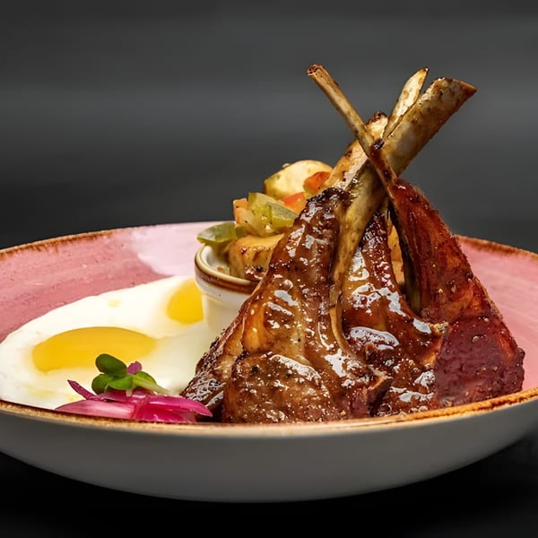 Just Brunch lamb chops with fried eggs, roasted potatoes, and pickled onions on a pink plate.