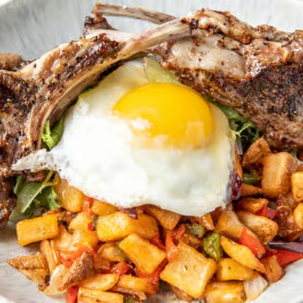 Just Brunch lamb chops with a fried egg, home fries, and greens on a white plate.