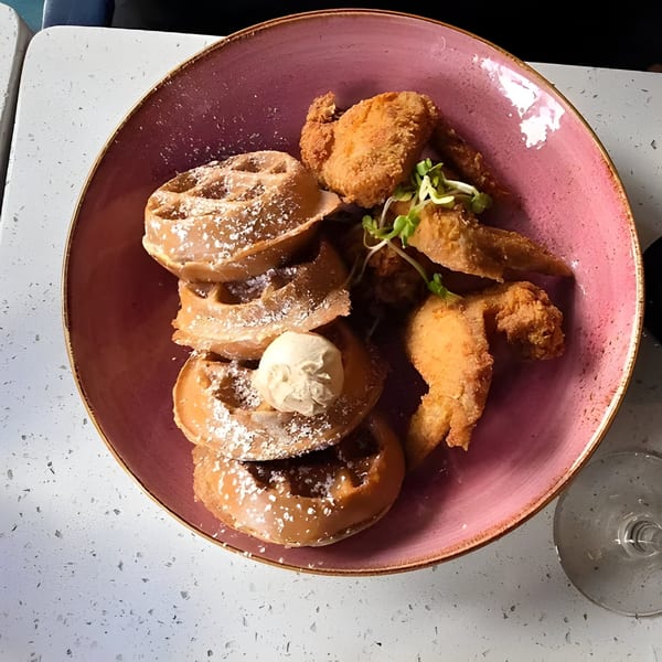 Just Brunch's chicken and waffles, with powdered sugar and a dollop of butter, in a pink bowl.
