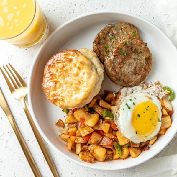 Just Brunch plate with sunny-side up egg, sausage patties, biscuit, home fries, and orange juice.