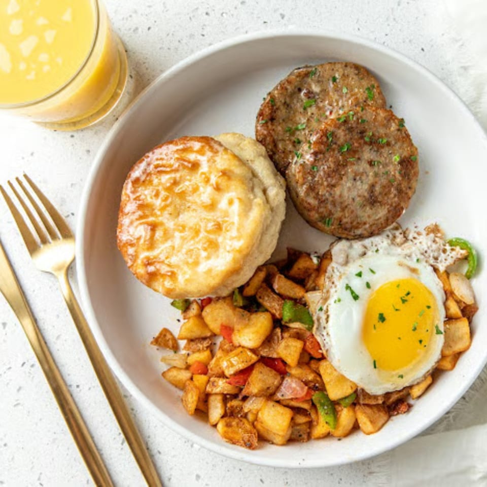 Just Brunch plate with sunny-side up egg, sausage patties, biscuit, home fries, and orange juice.