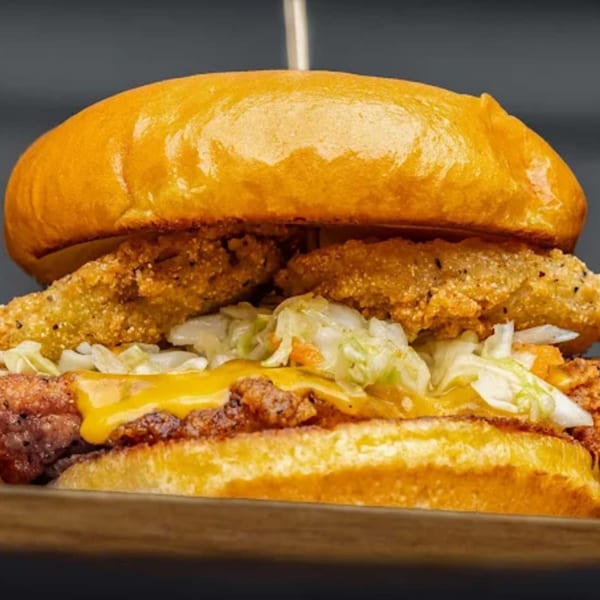 Close-up of a fried chicken sandwich with melted cheese, coleslaw, and pickles on a brioche bun.