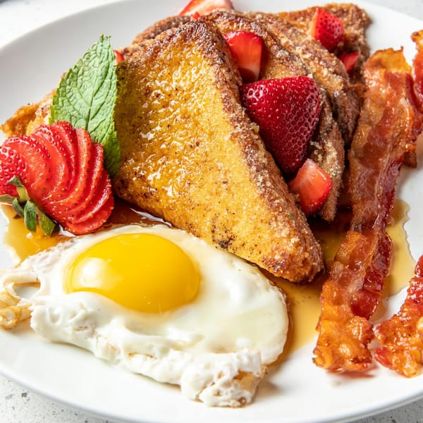 Just Brunch's French toast with strawberries, bacon, a fried egg, and mint on a white plate.