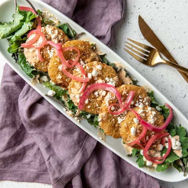Fried green tomatoes with pickled onions, feta, and sauce on a bed of greens.