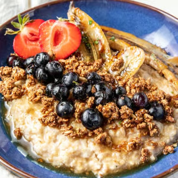 Just Brunch oatmeal with blueberries, granola, sliced strawberries, and caramelized bananas in a blue bowl.